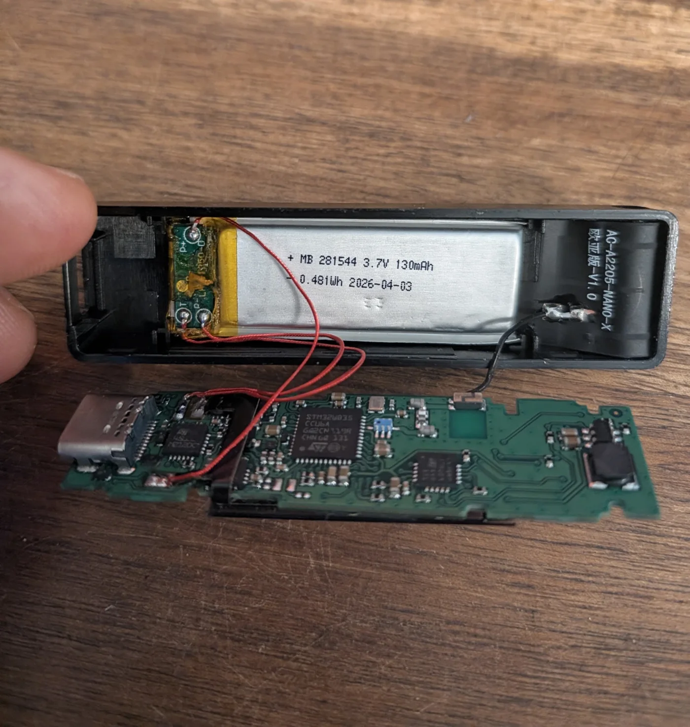 Ledger Nano X abierto compartido como el hallazgo europeo: cables rojos soldados a la placa de protección de la batería y un cable coaxial negro soldado a la carcasa, que llevan a una placa de circuito verde con lo que parece una segunda placa debajo